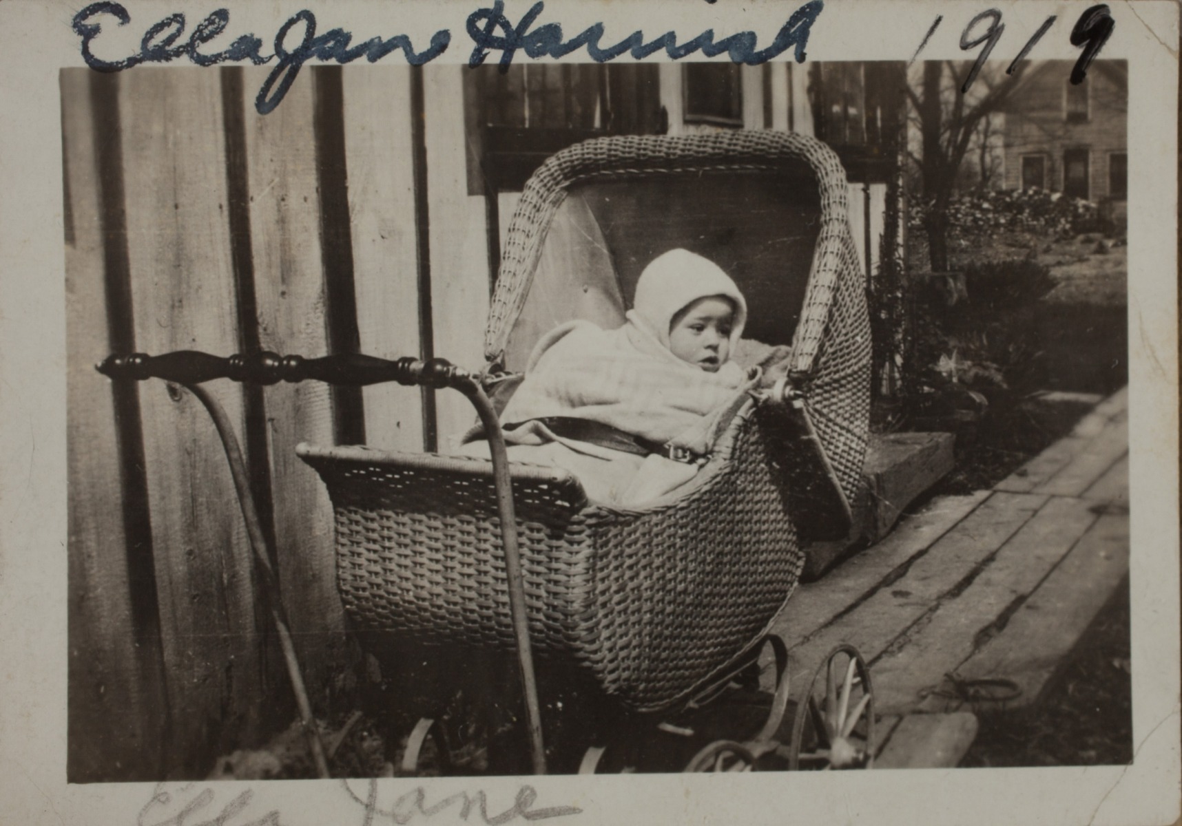 1919 Ella Jane Harnish" in baby buggy on wooden walkway. note she is strapped in with a belt.